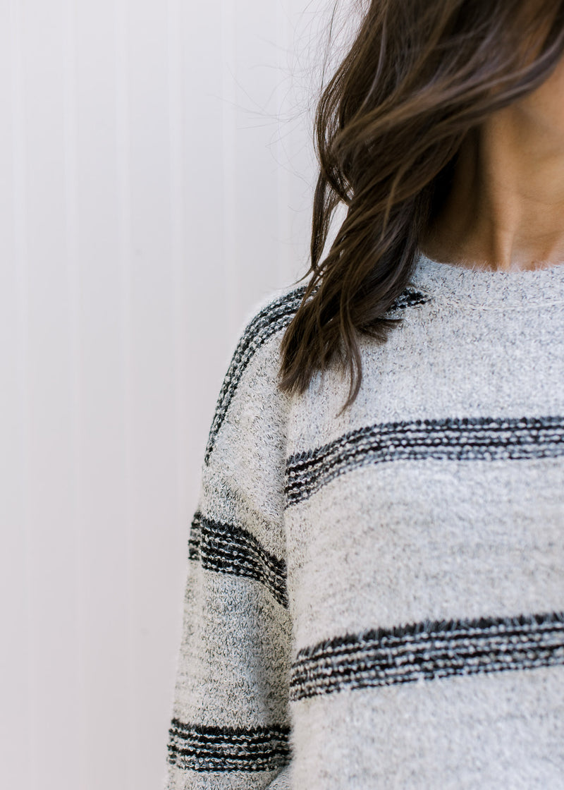 Close up of black stripes on a gray sweater with long sleeves and a round neck. 