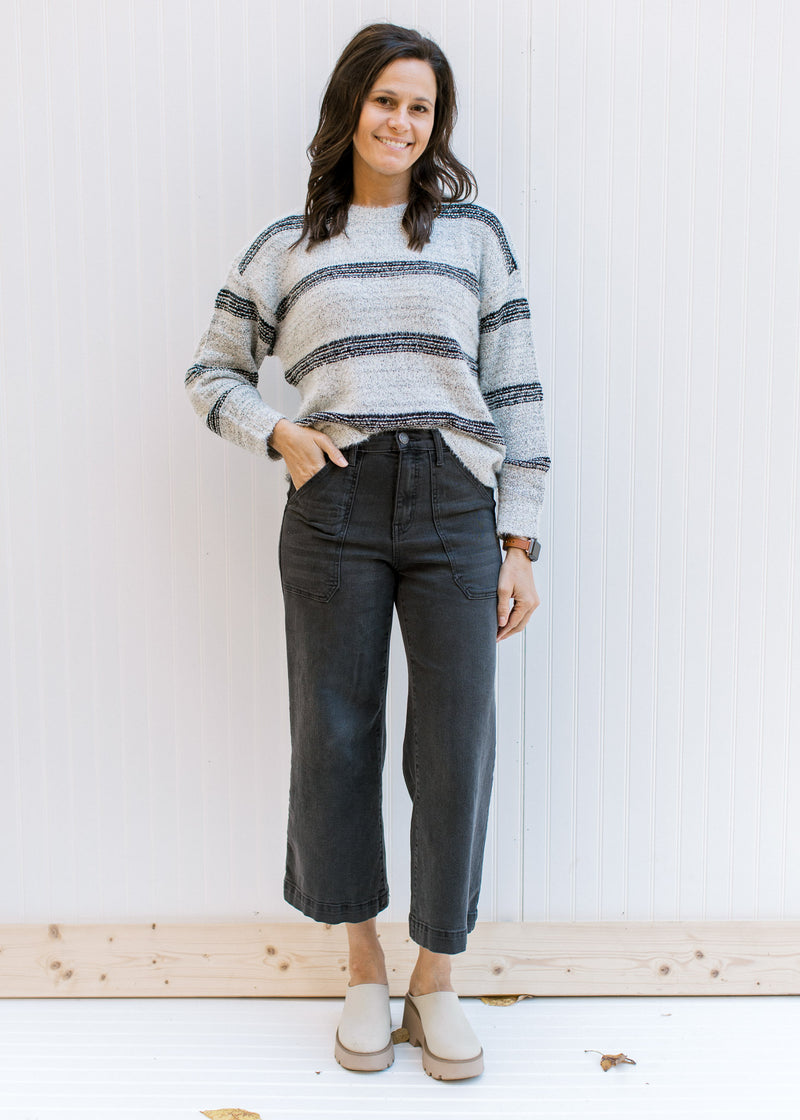 Model wearing jeans and mules with a gray sweater with black stripes, long sleeves and round neck. 