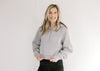 Model wearing a gray hoodie with a 1/4 zip, long sleeves and a front pouch pocket.