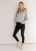 Model wearing black pants and a gray pullover with a 1/4 zip, long sleeves and a front pouch pocket.