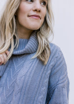 Close up of cable knit and cowl neck on a blue/gray long sleeve sweater with an acrylic material.