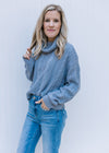 Model wearing jeans and a blue/gray sweater with a cowl neck, extended shoulder and long sleeves.