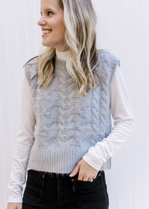 Model wearing a white top with a gray ultra soft vest with a round neck and cable knit material. 