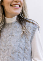 Close up of cable knit and round neck on a gray ultra soft sweater vest over a white top. 
