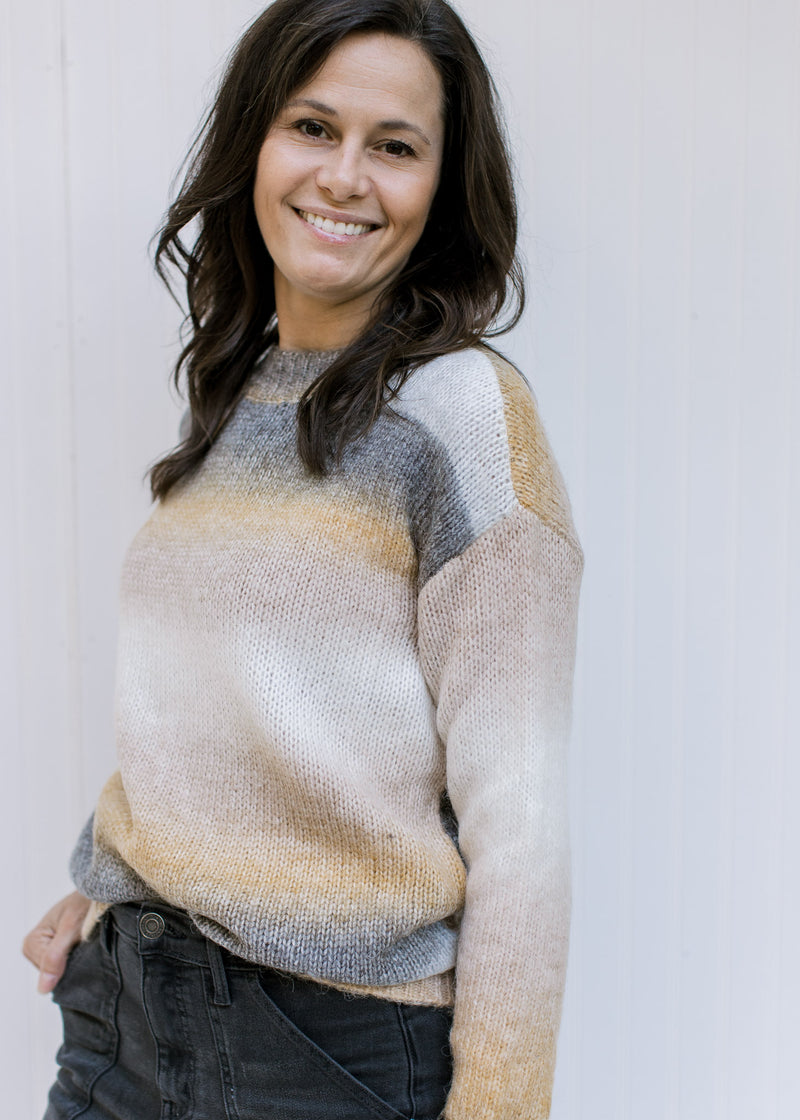 Model wearing a gray, cream and mustard ombre sweater with a ribbed detail and long sleeves. 