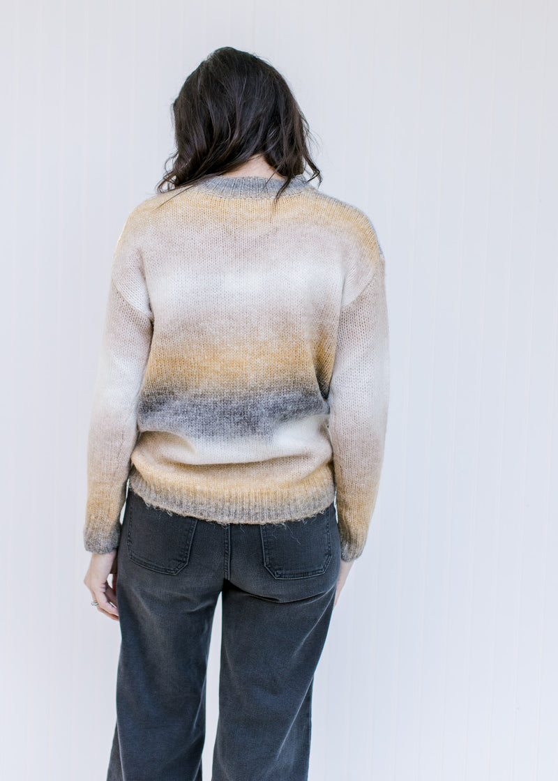 Back view of Model wearing a long sleeve gray, cream and mustard ombre sweater with a ribbed detail.