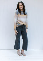 Model wearing jeans and booties with a gray, cream and mustard ombre sweater and long sleeves. 