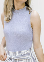 Close up view of Model wearing a ribbed gray sleeveless body suit with a mocked neckline. 