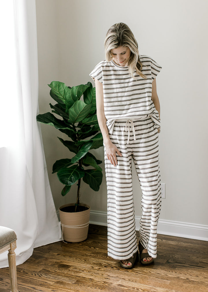 Model wearing a lounge set with gray and white stripes, short sleeve top and tie wide leg pants. 