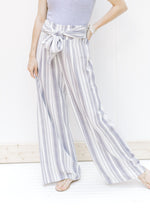 Model wearing gray and white striped wide leg pants with an elastic waist and tie front detail. 