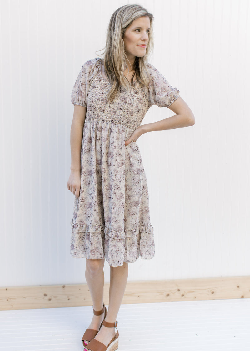 Model wearing a gray slightly above the knee floral dress with a smocked bodice and  short sleeves.