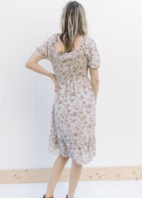 Back view of Model wearing a gray floral dress with a smocked bodice and sheer bubble short sleeves.