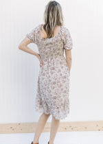Back view of Model wearing a gray floral dress with a smocked bodice and sheer bubble short sleeves.