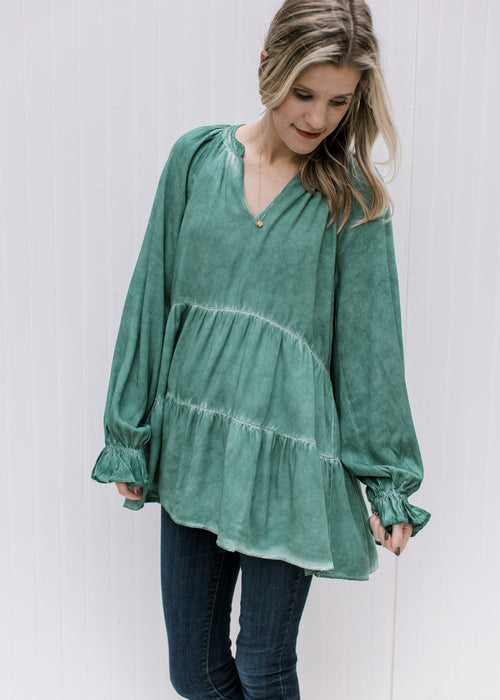 Model wearing a green v-neck top with wide long sleeves, tiered layers and a tunic length 