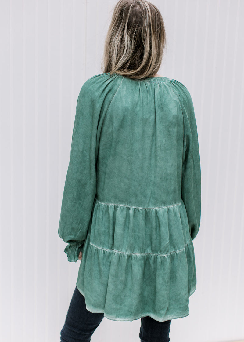 Back view of Model wearing a green top with wide long sleeves, tiered layers and a tunic length 
