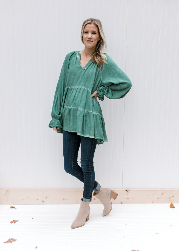 Model wearing booties, jeans and a green top with wide long sleeves and a tunic length.