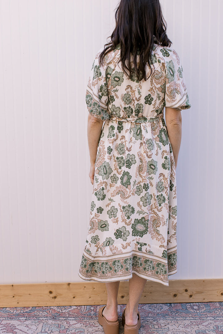 Back view of a cream midi with green and tan floral, bubble short sleeves and tie at waist. 