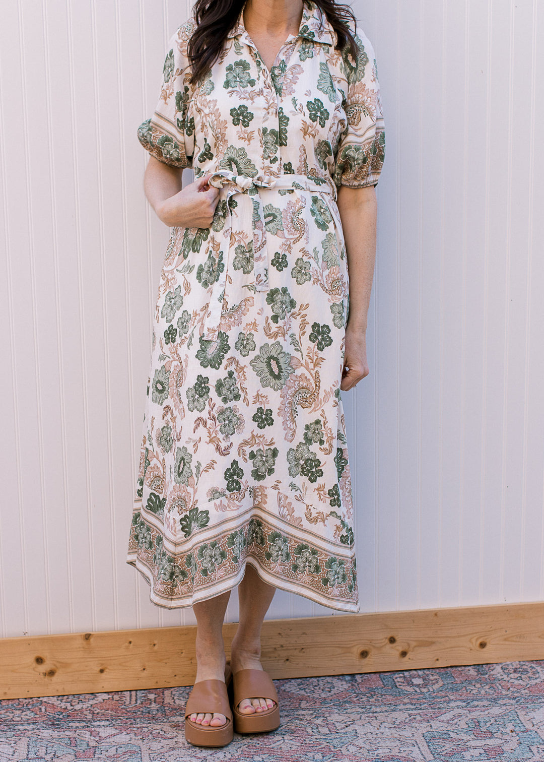 Model wearing heels and a cream midi with green and tan floral, button-front and tie at waist.