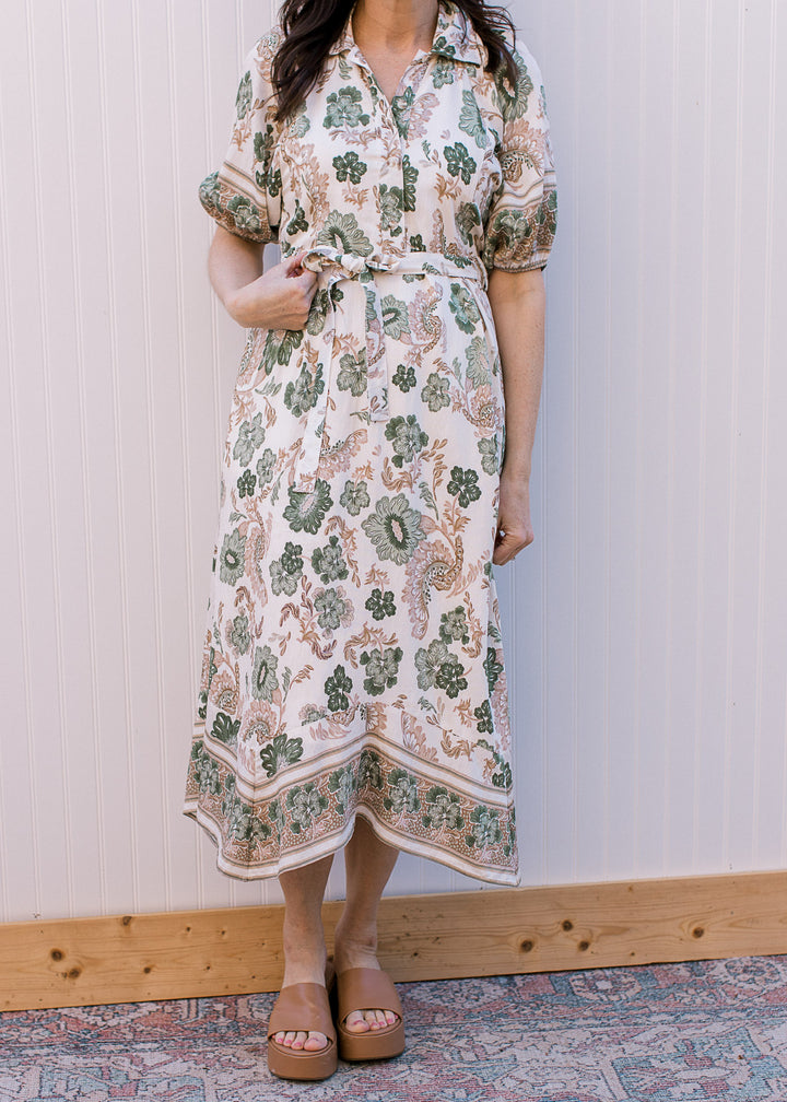 Model wearing heels and a cream midi with green and tan floral, button-front and tie at waist.