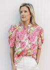 Model wearing a cream top with pink and green floral print, pleated shoulders and a ruffle neck.