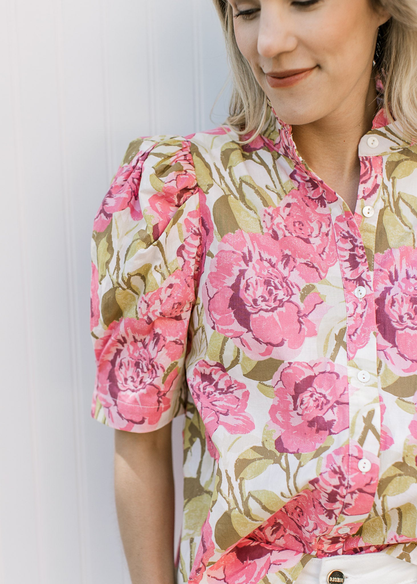 Close up of pleated short shoulders and buttons on a cream top with pink and green floral.