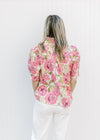 Back view of Model wearing a cream top with pink and green floral print, buttons and a ruffle neck.