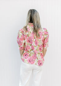 Back view of Model wearing a cream top with pink and green floral print, buttons and a ruffle neck.
