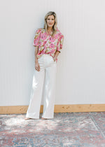 Model wearing white jeans and a cream top with pink and green floral print and buttons. 