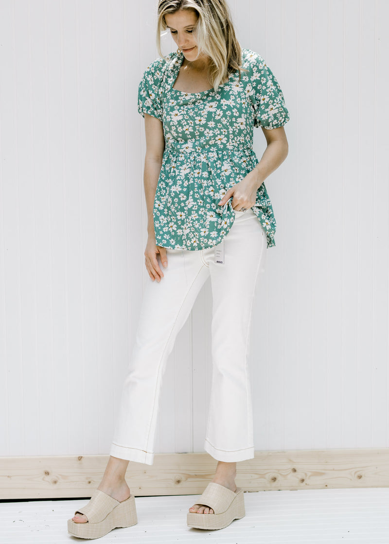 Model wearing white jeans, wedges and  a green top with a white floral pattern and a square neck. 