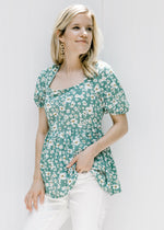 Model wearing a green top with a white floral pattern, square neckline and smocked back with a tie. 
