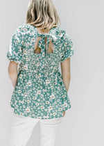 Back view of green top with white floral pattern bubble short sleeves and a tie at the neck. 