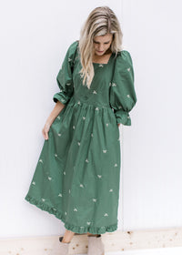 Model wearing a green midi with cream embroidered bows, a square neck, 3/4 poet sleeves and booties.