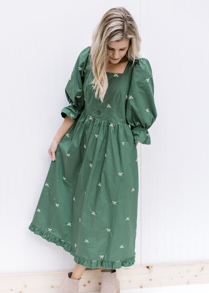 Model wearing a green midi with cream embroidered bows, a square neck, 3/4 poet sleeves and booties.
