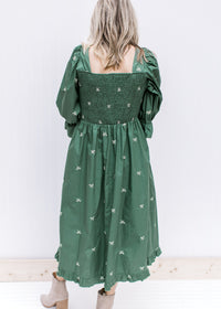 Back view of smocked back and square neckline on a green midi with cream embroidered bows. 
