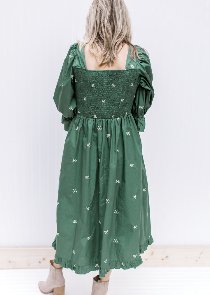 Back view of smocked back and square neckline on a green midi with cream embroidered bows. 