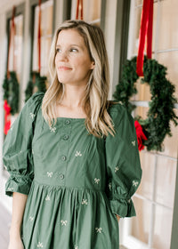 Model wearing a green dress with cream embroidered bows, a square Nike and 3/4 poet sleeves. 