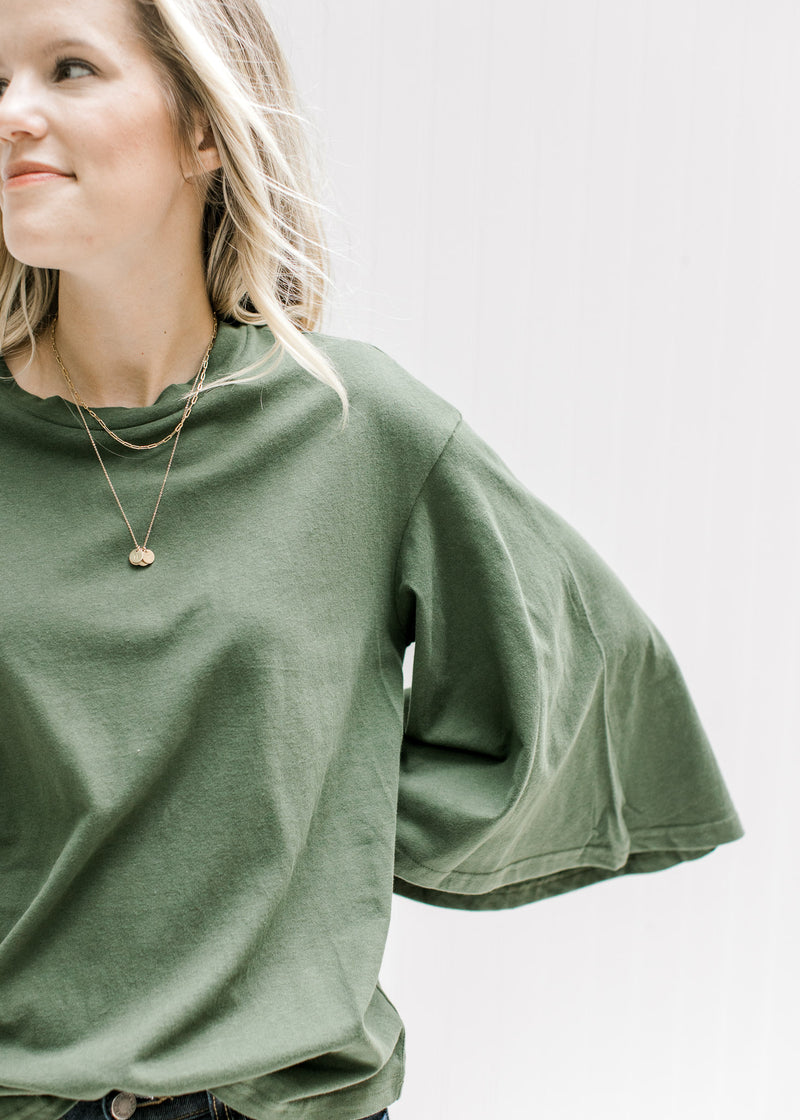 Close up of a 3/4 butterfly sleeve on an olive colored top with a round neck and a cotton material. 