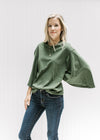 Model wearing jeans with an olive top with 3/4 butterfly sleeves, a round neck and a cotton material