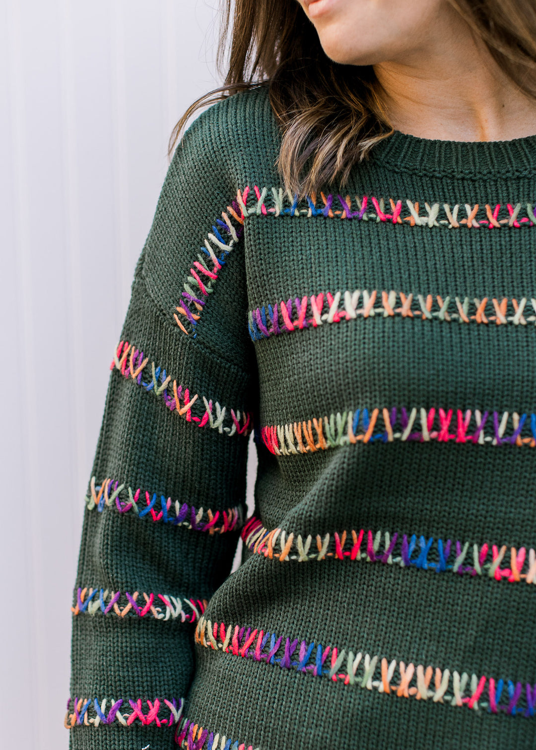 Close up of colorfully stitched stripes on a knit hunter green sweater with long sleeves. 