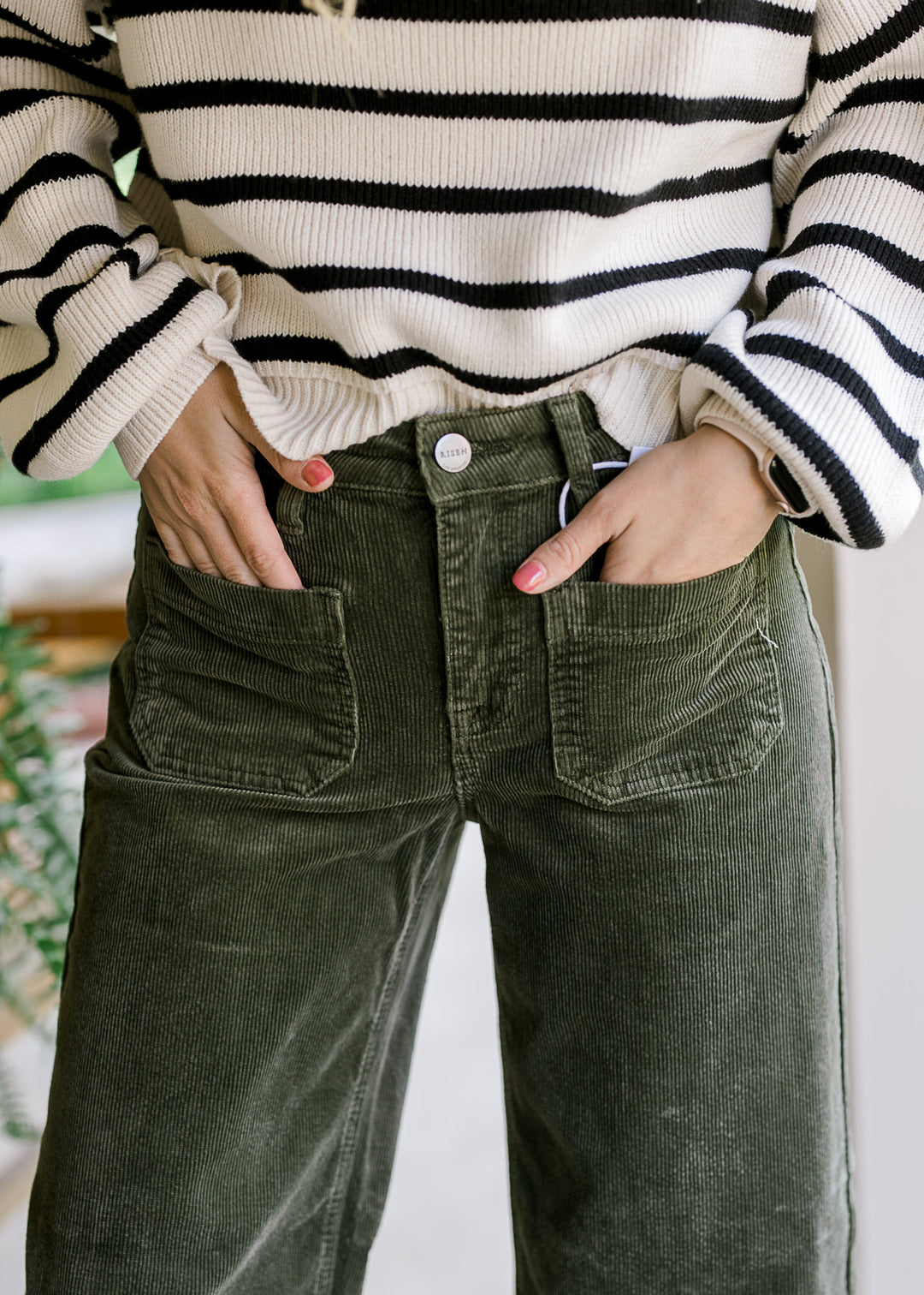 Close up of patch pockets on moss colored corduroy pants with traditional button closure. 