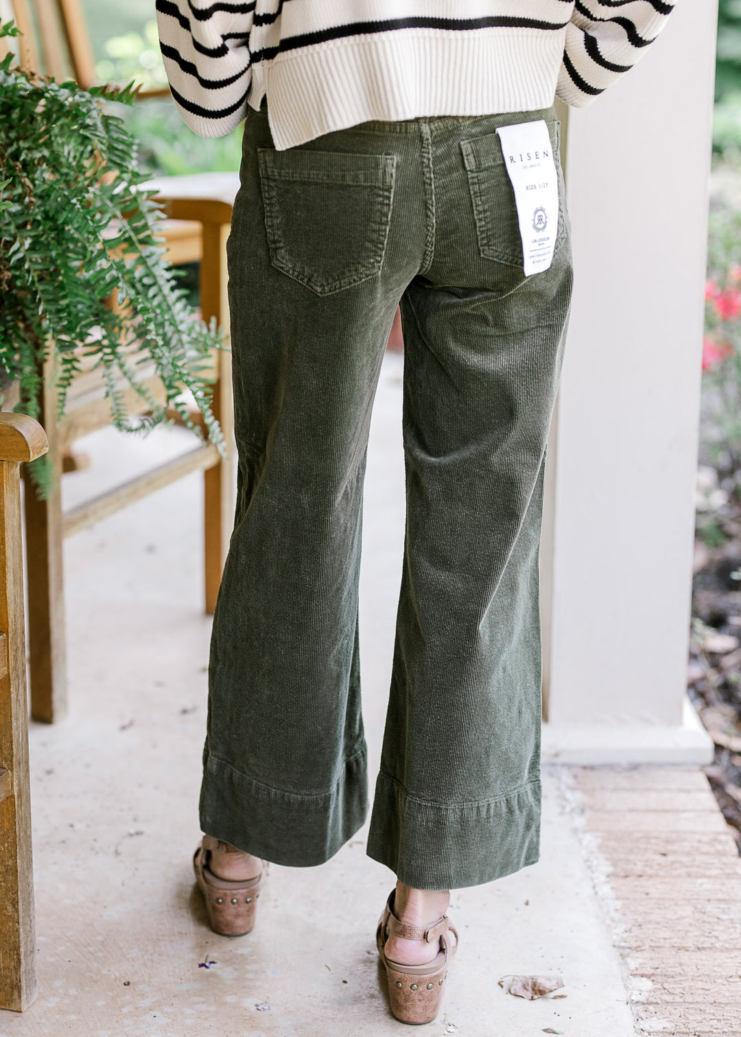 Back view of Model wearing green corduroy cropped pants with traditional button. 