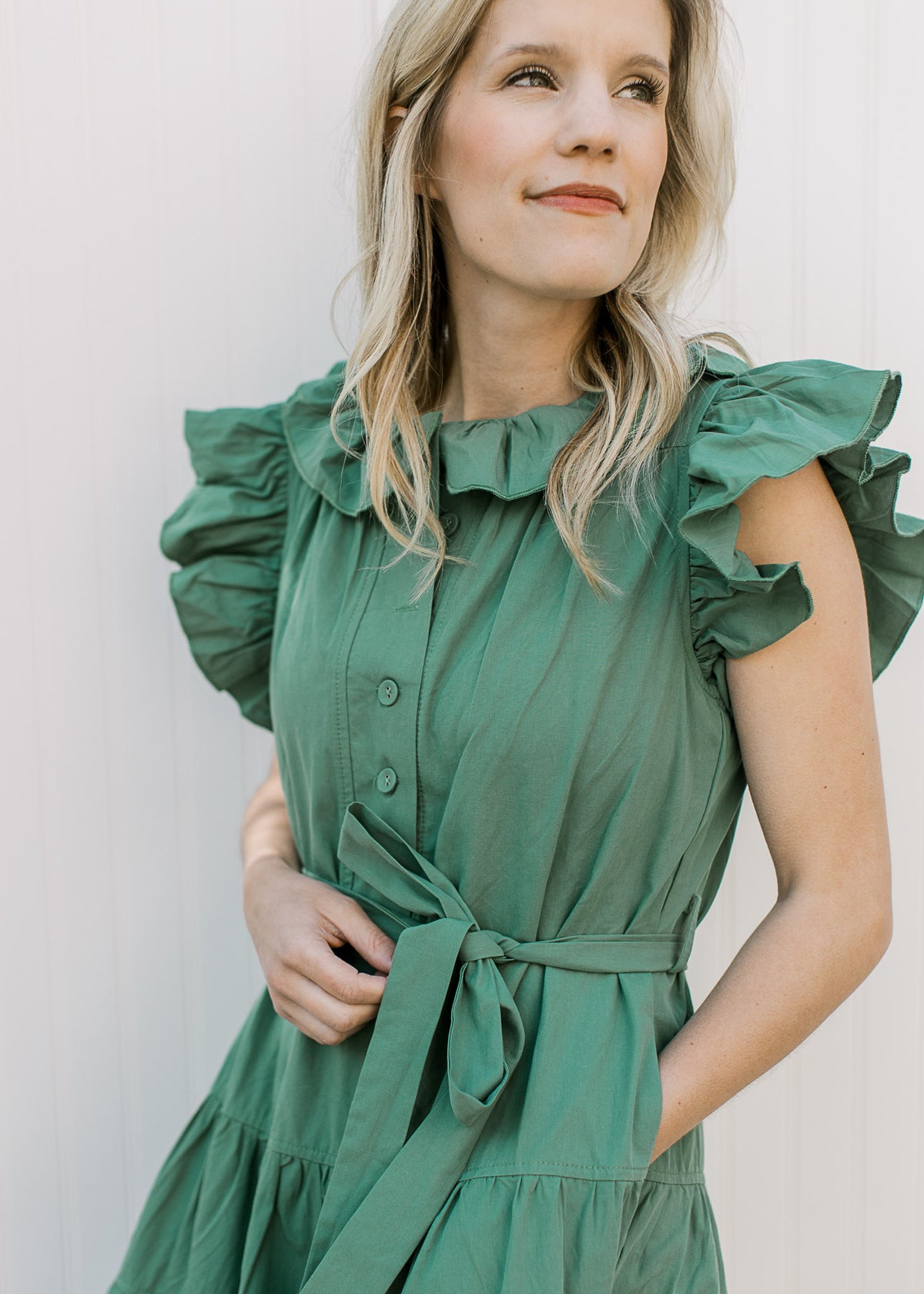Close up of tie waist, buttons ad ruffle at neck and sleeve of a deep green midi with pockets.