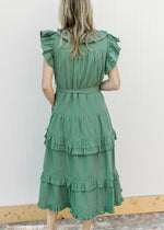 Back view of Model wearing a deep green midi with ruffle collar, sleeves and double ruffle on skirt.