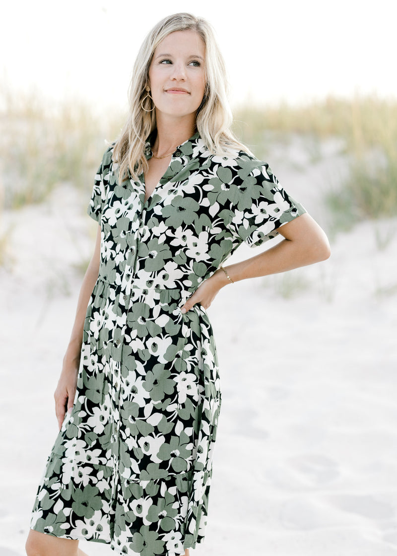 Model wearing an above the knee black dress with cream and green floral pattern and short sleeves.  