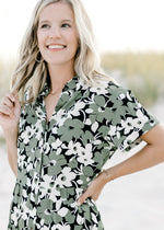 Close up view of button closure and short sleeves on a black dress with green and cream pattern. 