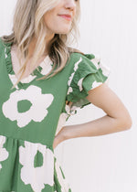 Close up of layered ruffle cap sleeves and ruffled v-neck on a green dress with cream flowers. 
