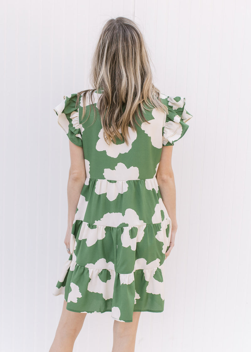 Back view of Model wearing a green dress with cream flowers, pockets and layered cap sleeves.