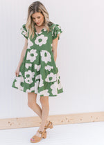 Model wearing heels with a green dress with cream flowers, pockets and layered cap sleeves.
