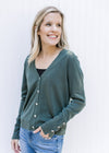 Model wearing a black shirt under a green long sleeve cardigan with flower rhinestone buttons. 