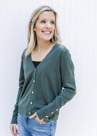 Model wearing a black shirt under a green long sleeve cardigan with flower rhinestone buttons. 